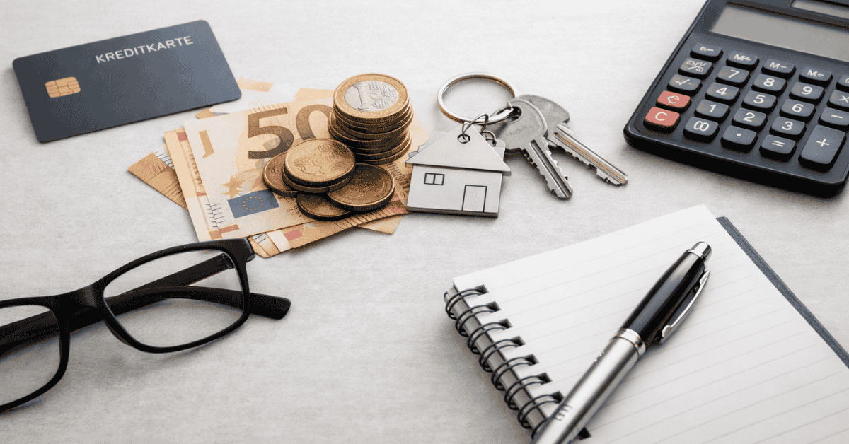 Kreditkarte, Euro-Banknoten und Münzen neben Hausschlüssel, Taschenrechner und Notizbuch als Symbol für Zinsen, Kredite und finanzielle Planung in Deutschland.